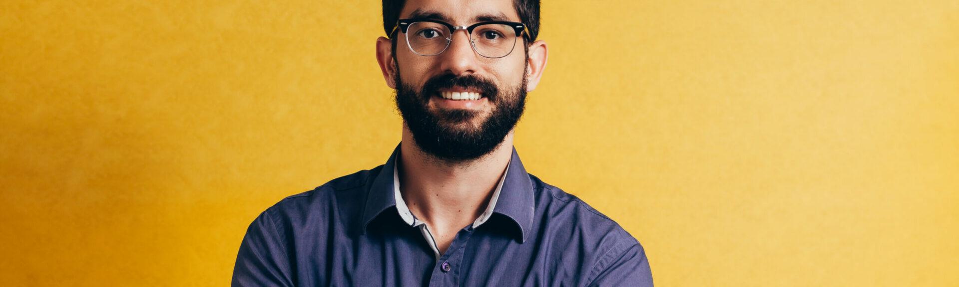 Portrait of a smiling bearded man in eyeglasses looking at camera isolated over yellow background